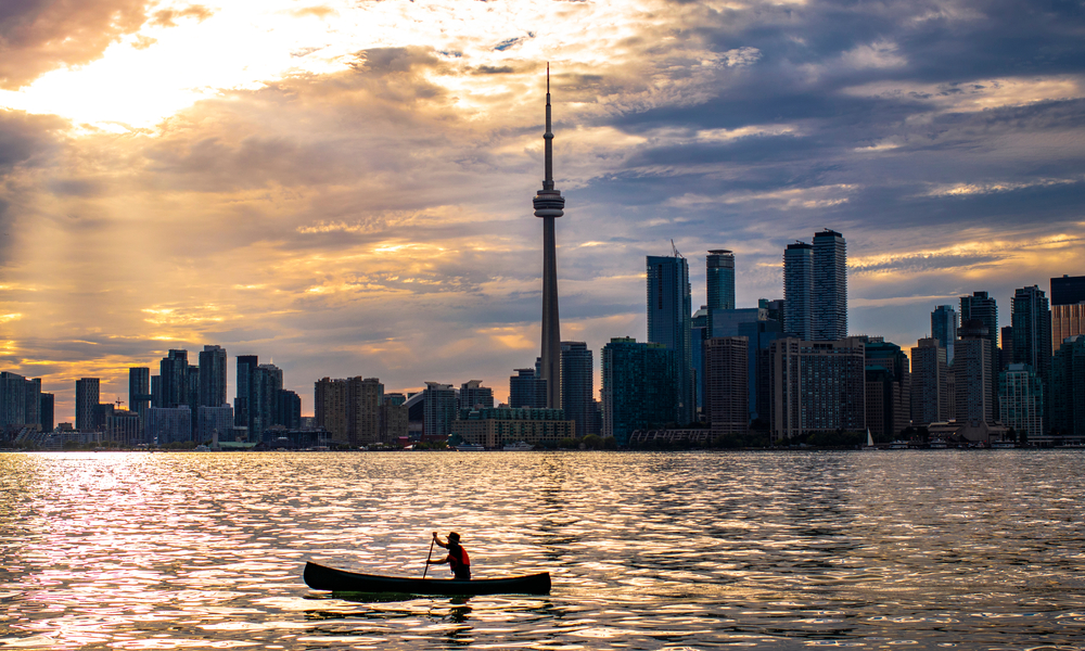 Top Domestic Destinations in Canada: Canoe being paddled past Toronto skyline at sunset.