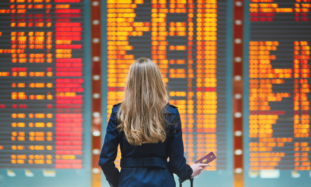  How to find cheap last minute flights: Young woman in international airport looking at the flight information board, checking her flight