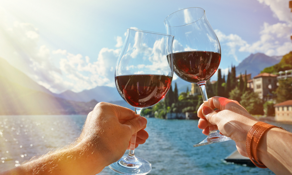 The most romantic places in Italy: Two wineglasses in the hands of a couple, overlooking Varenna town at the lake Como, Italy