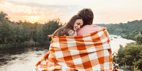 6 Under-the-Radar Romantic Getaways:Loving couple wrapped in plaid sitting on mountain outdoors on sunset.