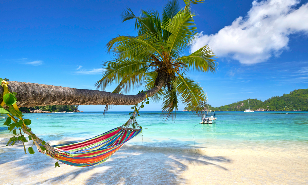 6 Under-the-Radar Romantic Getaways: Romantic cozy hammock in the shadow of coconut palm tree at tropical paradise ocean beach in bright sunny summer day 