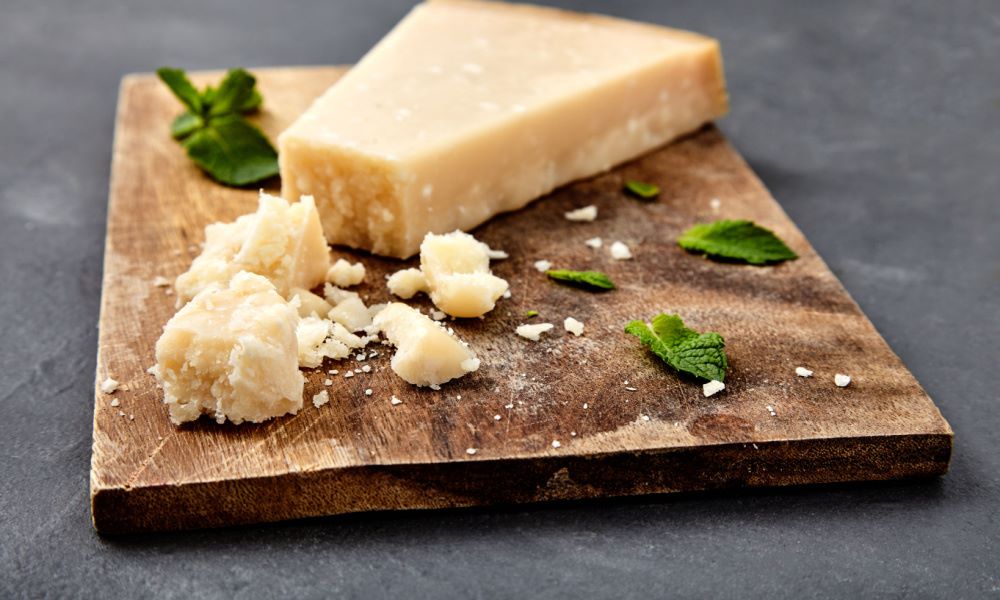 Pieces of parmigiano reggiano or parmesan cheese on wood board on stone background. Parmesan is hard cheese uses in pasta dishes, soups, risottos and grated over salads.