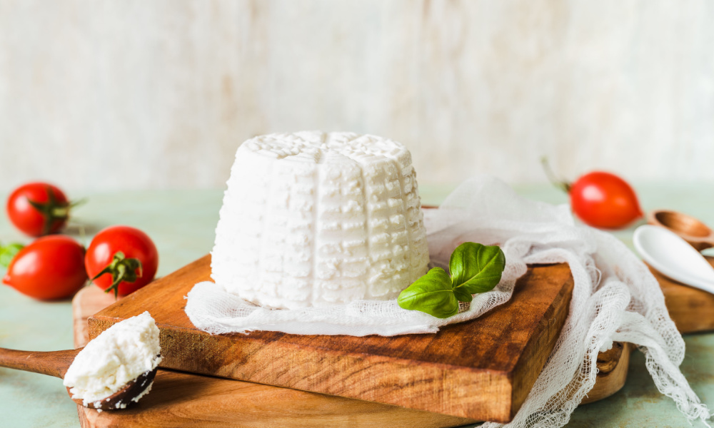 ricotta cheese on wooden base, teaspoon filled with ricotta cheese, basil, tomatoes blurred in the background