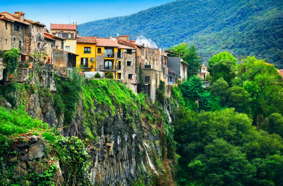 Castellfollit de la Roca, Garrotxa, Province of Girona, Catalonia, Spain, Europe. Beautiful scenic view, old houses over the huge basalt cliff and mountain covered with green wood at the background