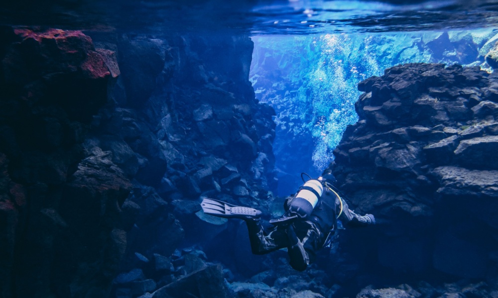 Divers scuba diving between two tectonic plates in Silfra, Iceland.