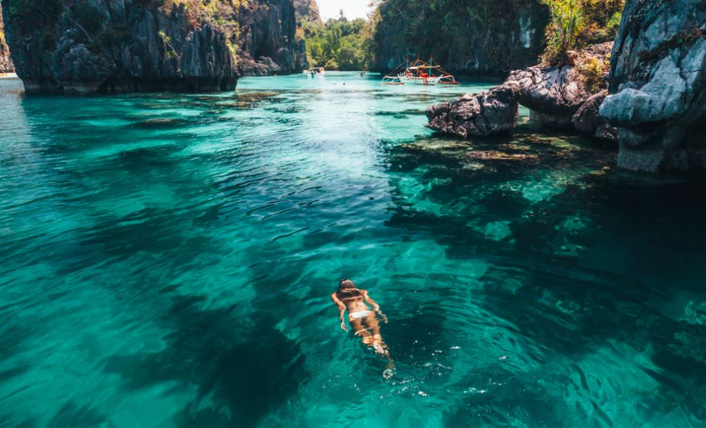 Young woman swimming in clear sea water in lagoon and looking at beautiful landscape. Travelling tour in Asia: El Nido, Palawan, Philippines.