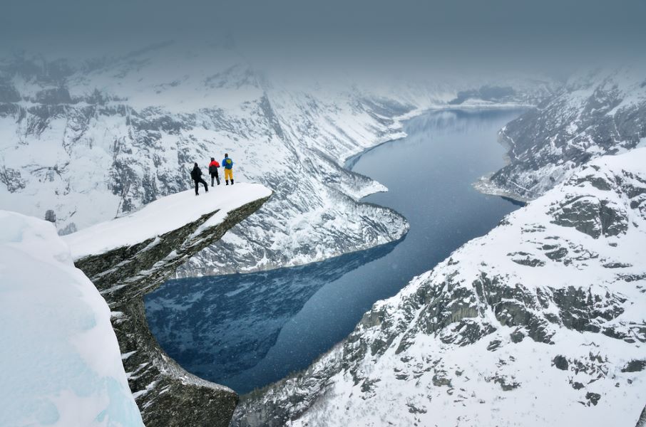 Tree young boys standing on famous Trolltunga rock in Norway and looking to the mountains